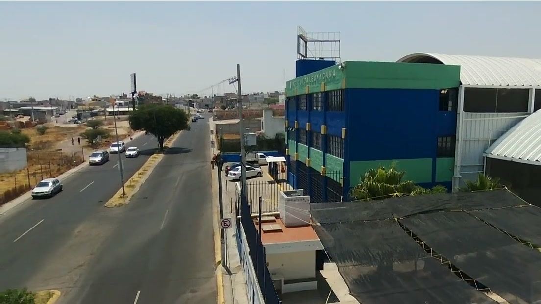 Vista aérea del instituto: edificio azul y verde, techos en arco y la avenida a un costado.